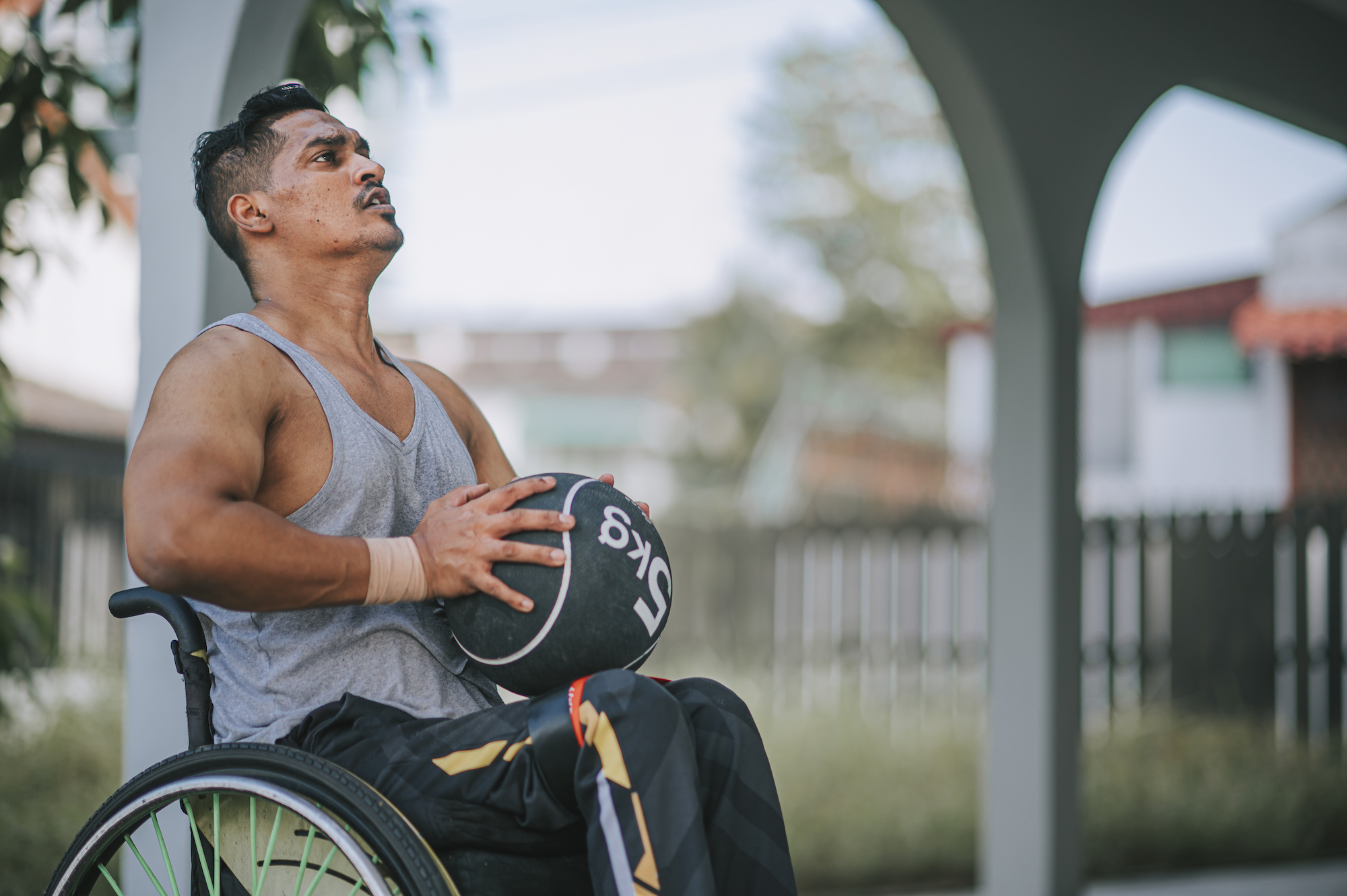 Man in a wheelchair outdoors holding a 5kg medicine ball in his lap