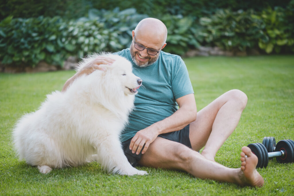 Man sitting on his lawn while smiling and patting his dog next to him