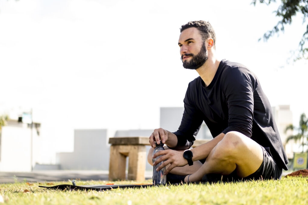 Man sitting cross-legged on the grass with his water bottle