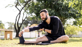 Young man smiling and sitting down in a park while stretching his right hamstring