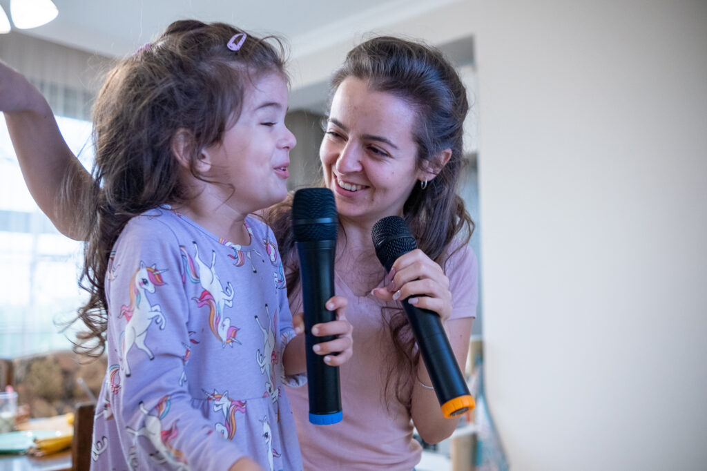 Mother and her young daughter singing with microphones in the living room