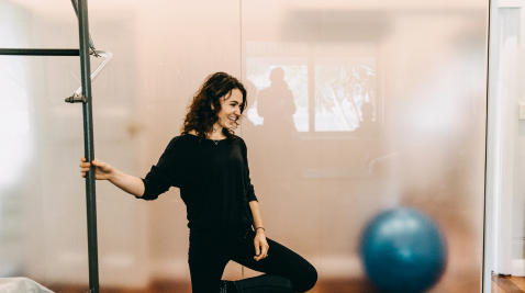 A woman in a yoga studio holding pole while smiling at the ground