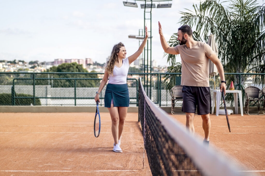 Young man and woman smiling and high-fiving on a clay tennis court