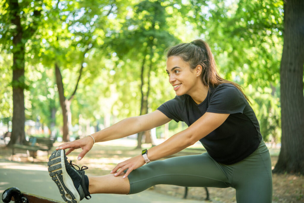Young woman smiling and stretching sitting down in a sunny park