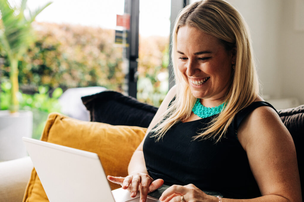 Woman smiling and sitting on the couch while using her laptop