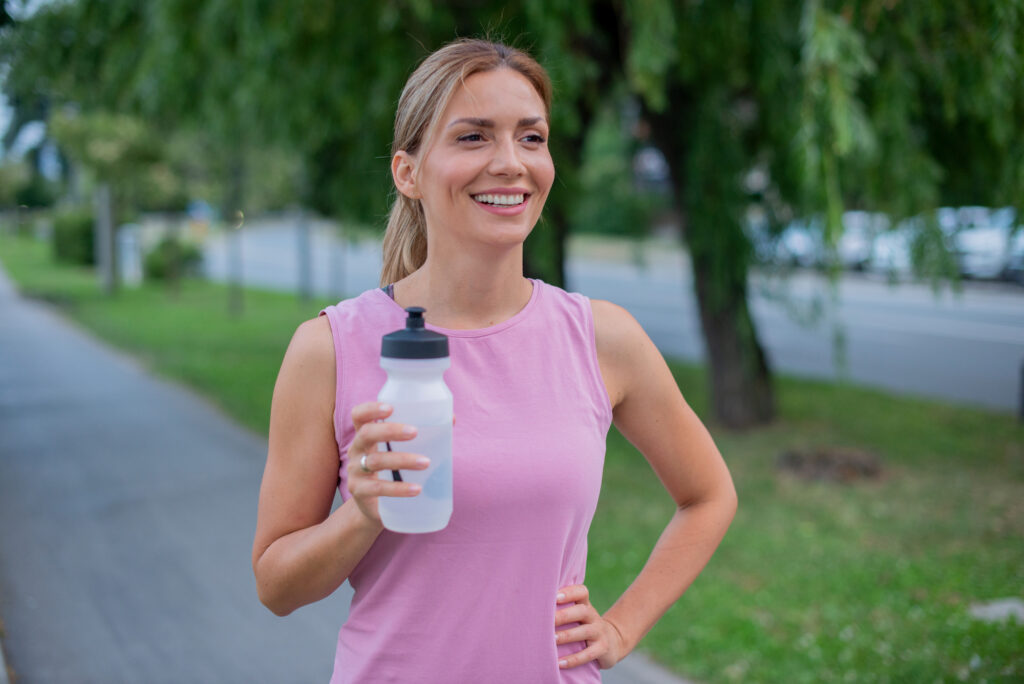 Young woman smiling and standing in a park with a water bottle in her hand