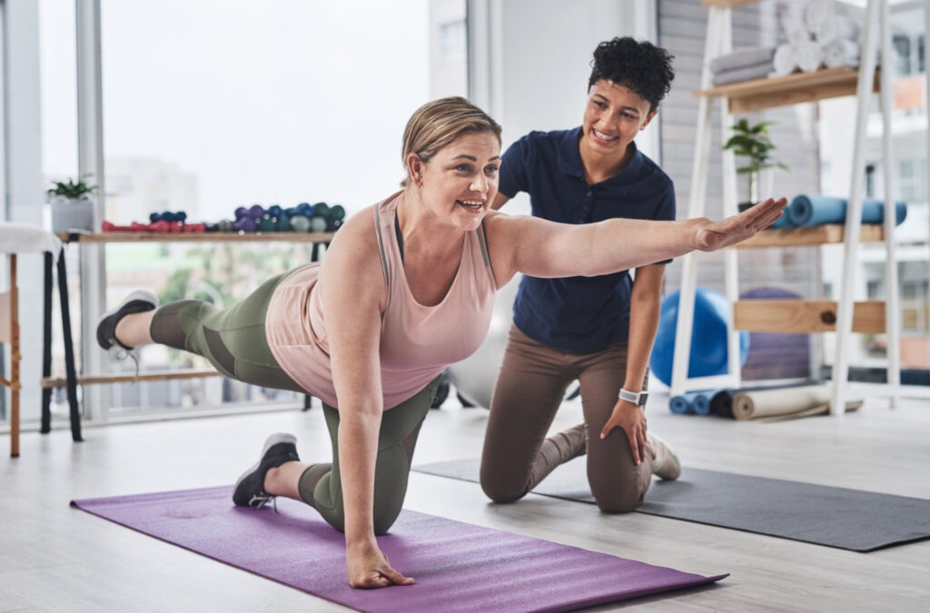 Woman helping another woman stretch on a mat at a physio