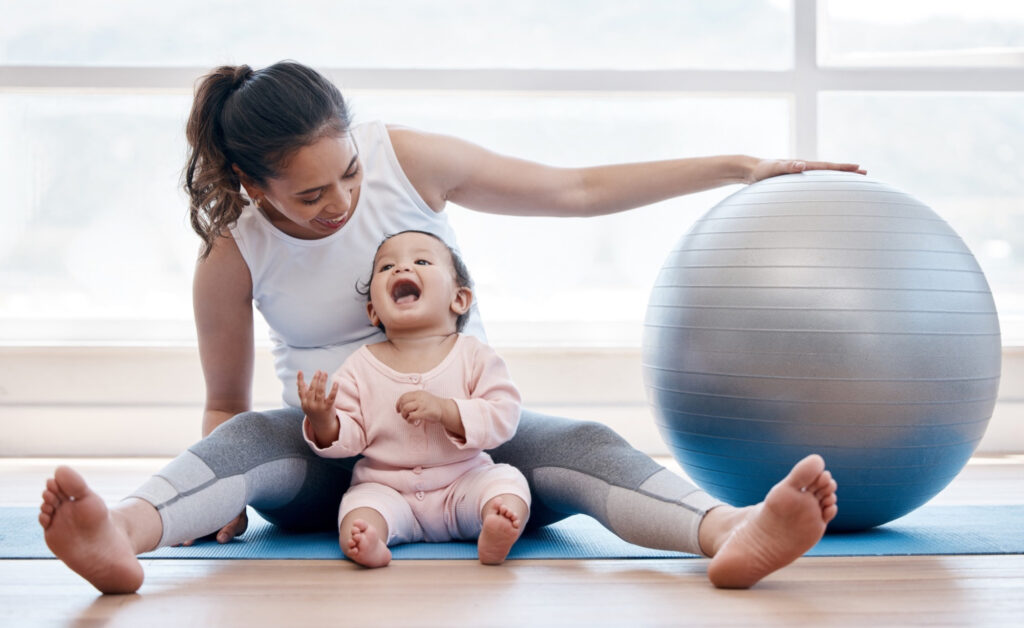 Mother smiling and sitting on a mat while at a physio with her young daughter
